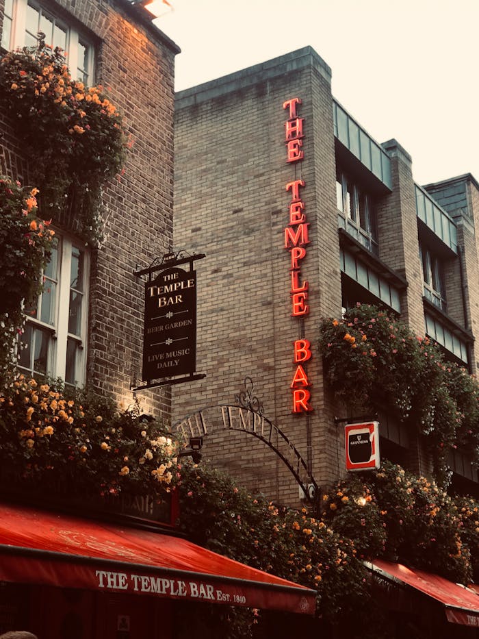 The vibrant facade of The Temple Bar in Dublin is adorned with flowers and neon signage, capturing its lively atmosphere.